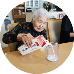 牛乳をコップに注ぐ年配女性の画像